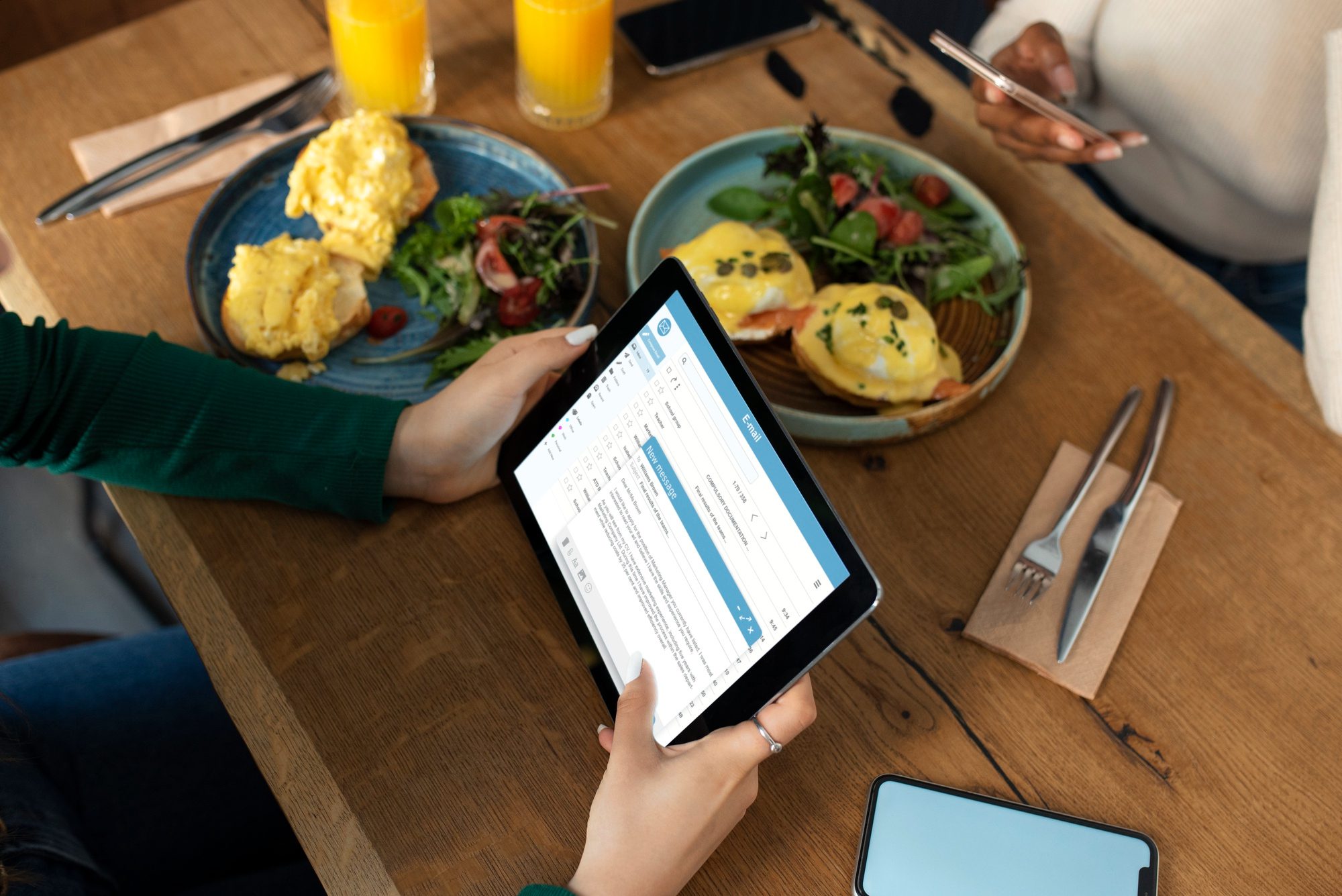 Person holding a tablet while having breakfast with eggs benedict and orange juice.