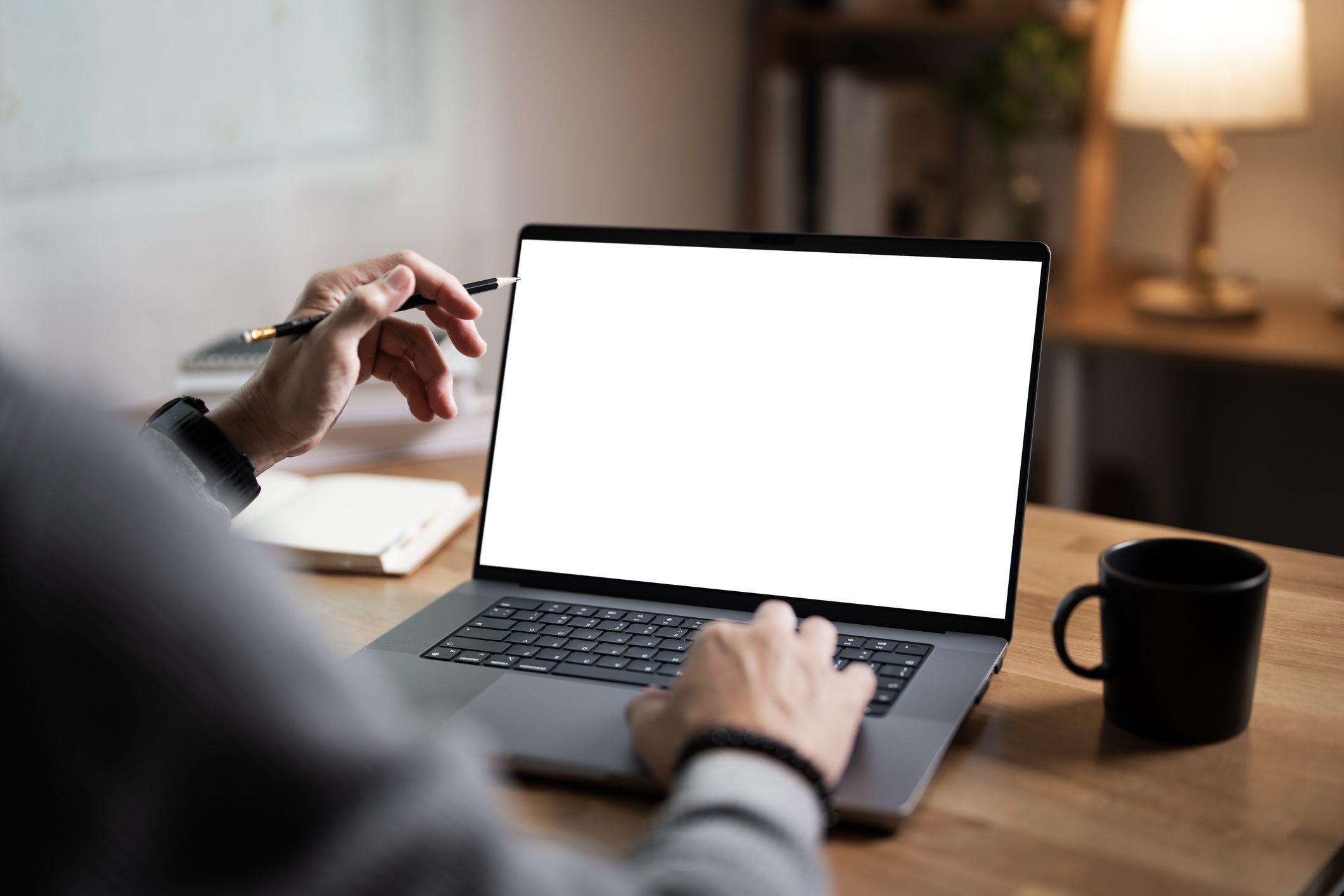 Person typing on a laptop with a blank screen and a coffee cup nearby.