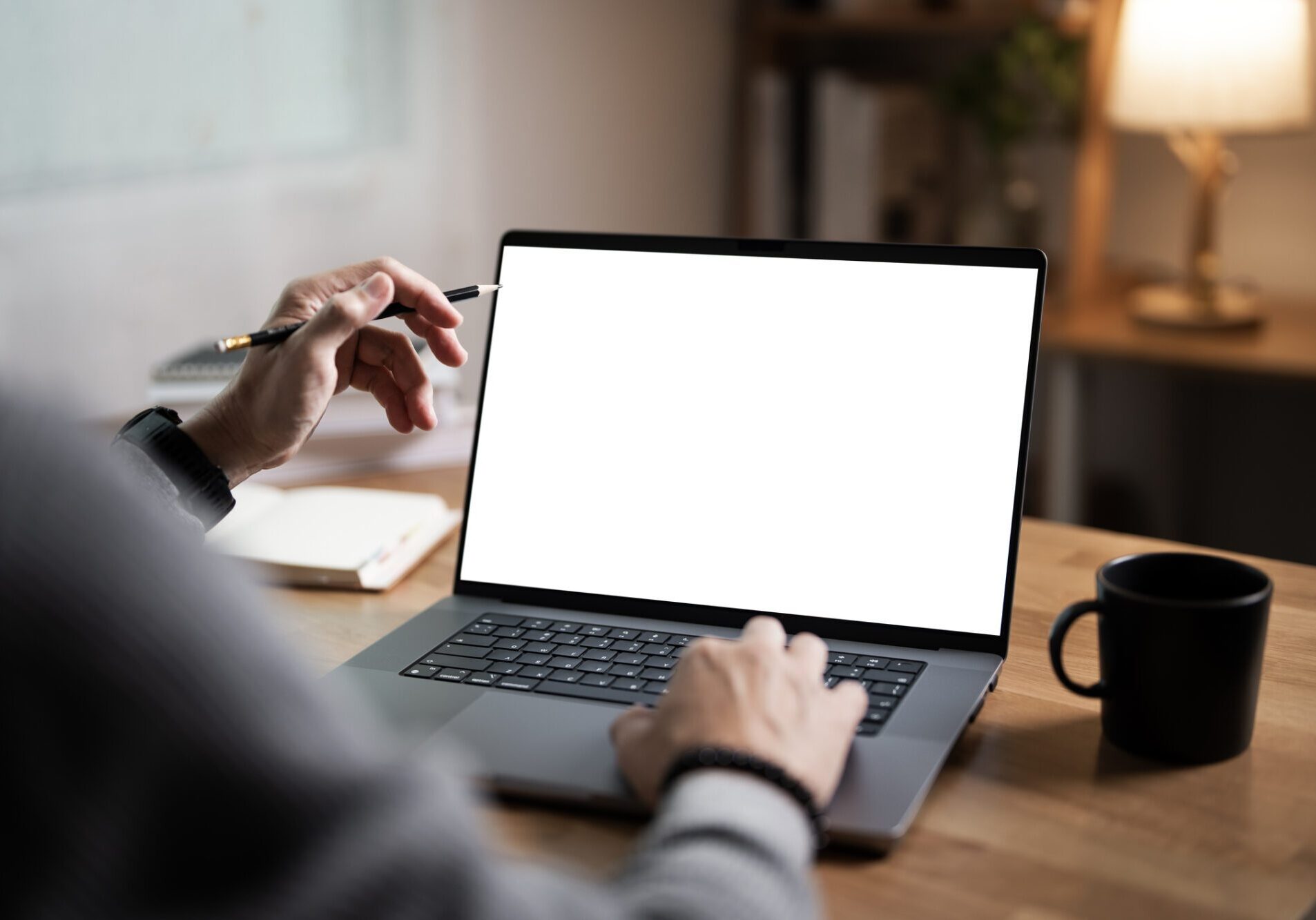 Person typing on a laptop with a blank screen and a coffee cup nearby.